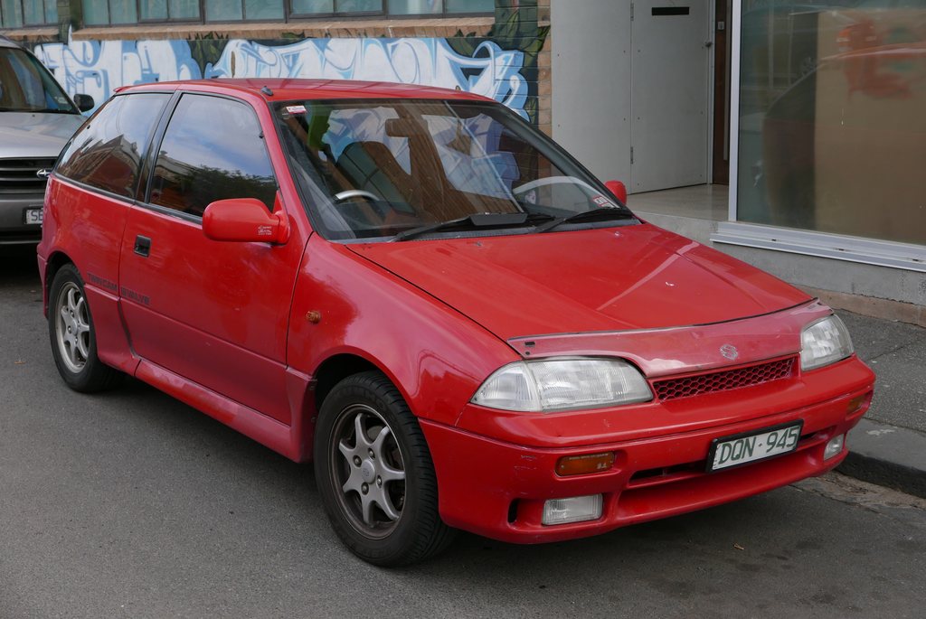 Front three-quarter period reference of a red 1989 Suzuki Swift GTi three-door hatchback parked on a street.